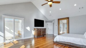 Ein geräumiges Schlafzimmer mit Holzdielenboden, einem großen Bett, einem Deckenventilator und einem an der Wand montierten Fernseher.
