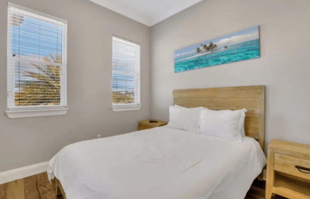 A bedroom with a large bed, two bedside tables, and a painting of a beach scene.