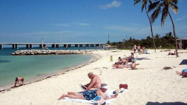 A beach with people sunbathing, a pier in the background, and palm trees. - Captain & Mermaid's Diamond #BP25 (Big Pine Key)