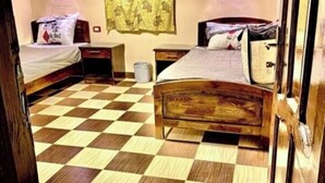 Ein Zimmer mit Schachbrettboden, zwei Betten, einem Nachttisch, einer Lampe und einem Wandvorhang.