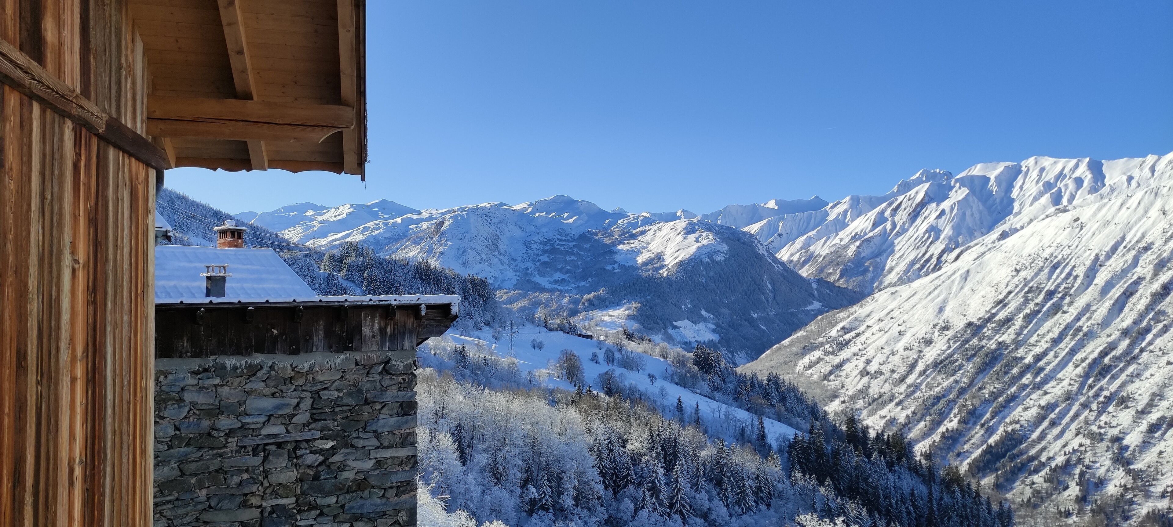 Blick auf Berge mit schneebedeckten Gipfeln und ein Steinhaus mit Holzziegeldach.