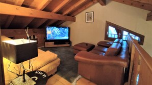 Una habitación acogedora en el ático con techo de madera, televisión, sofá y ventana.