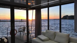 A modern room with a large window overlooking a body of water at sunset. - Hausboat Kamien Pomorski on the Water (Kamien Pomorski)