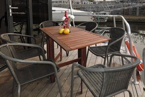 Ein Holztisch mit Stühlen auf einer Holzterrasse, eine Saucenflasche und eine Vase mit Blumen.