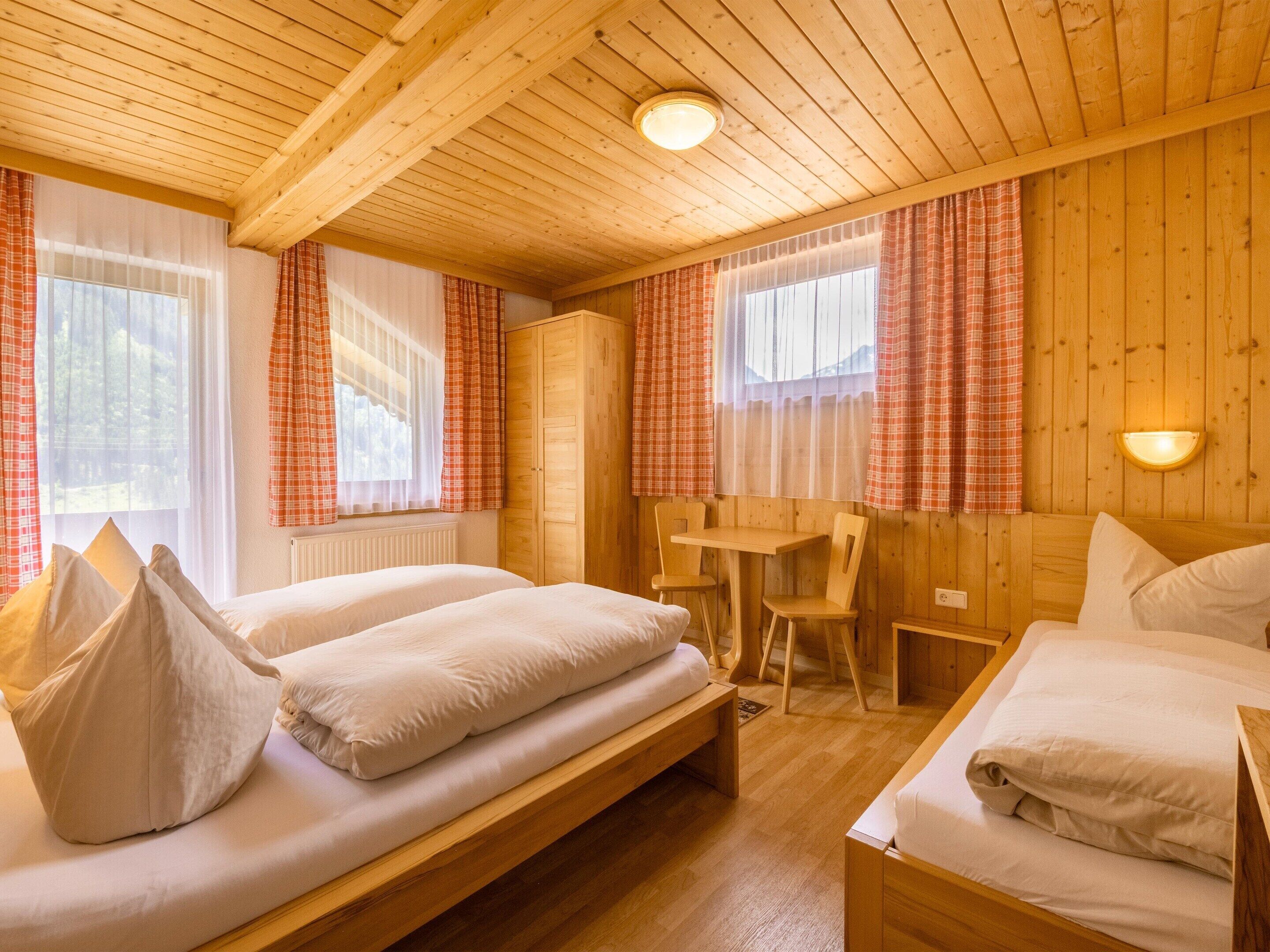 A wooden cabin room with two beds, a desk, and a chair.