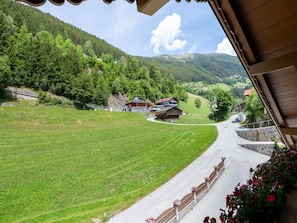 Blick auf eine Landstraße, die zu einem Dorf mit Häusern und einem Berg im Hintergrund führt.