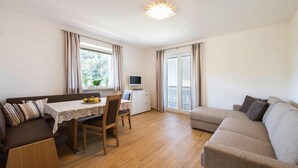 A modern living room with a sofa, a dining table with chairs, a TV, and a window with curtains. - Apartment in Dorf Tirol Near Tirol Castle (Tirolo)