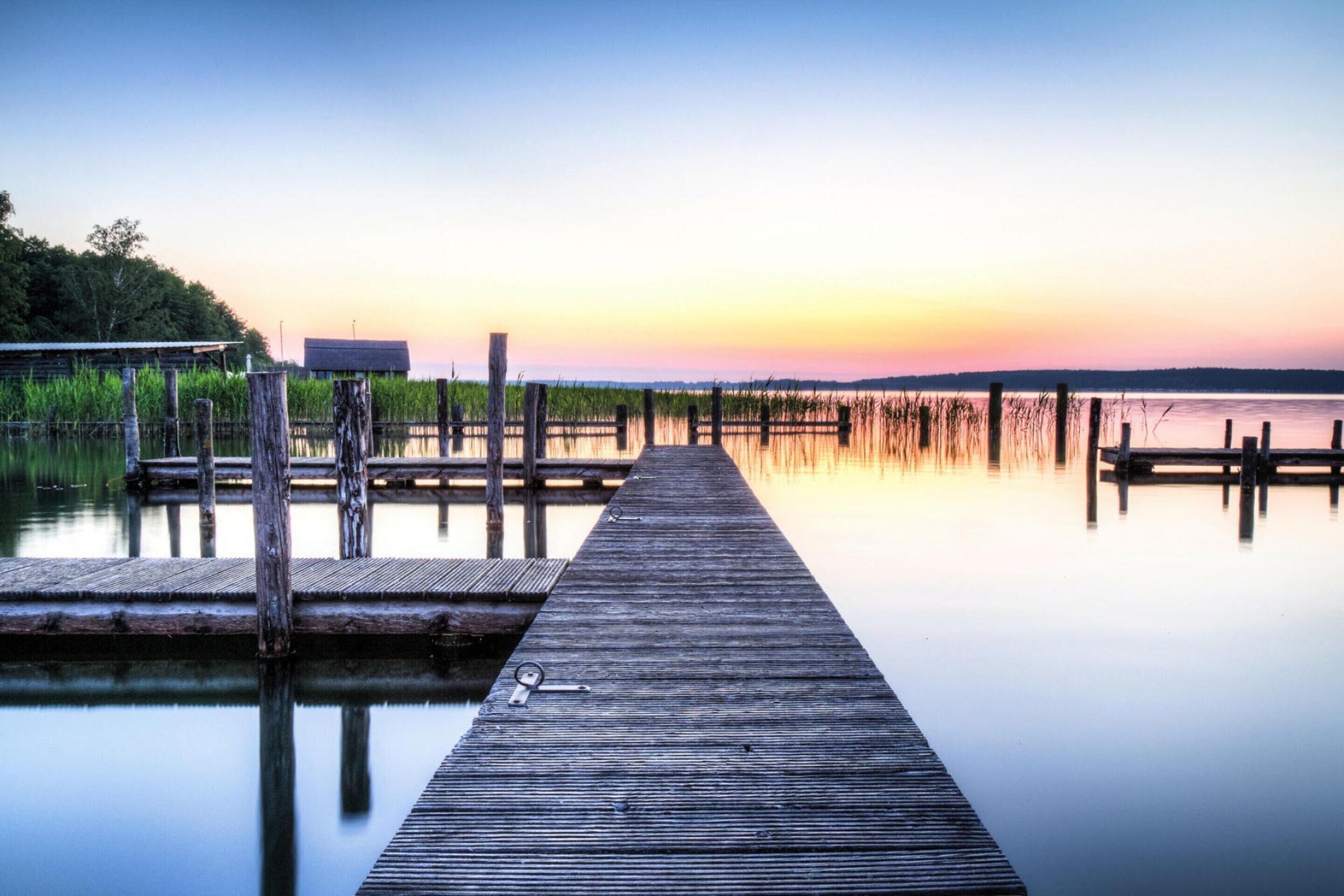 Une jetée en bois s’étendant sur une étendue d’eau calme, avec un coucher de soleil en arrière-plan.