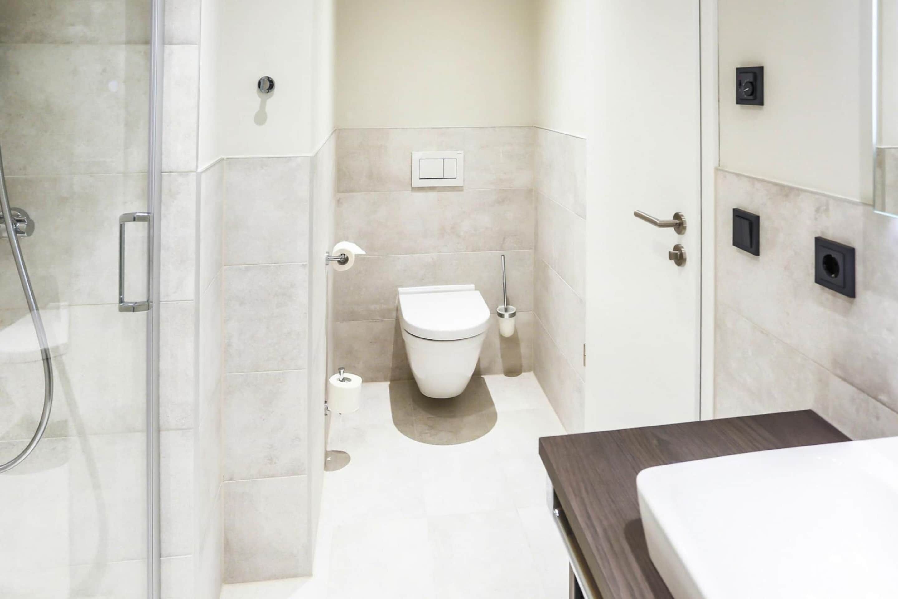 A modern bathroom with a glass shower enclosure, a toilet, and a sink with a dark countertop.