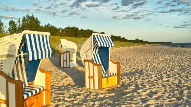 Beach chairs with striped covers and wooden frames on a sandy beach. - Luxushaus Boddenkuste mit Sauna (Fuhlendorf)
