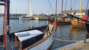 A marina with several boats docked, including a sailboat and a wooden boat with a cabin. - Luxushaus Boddenkuste mit Sauna (Fuhlendorf)