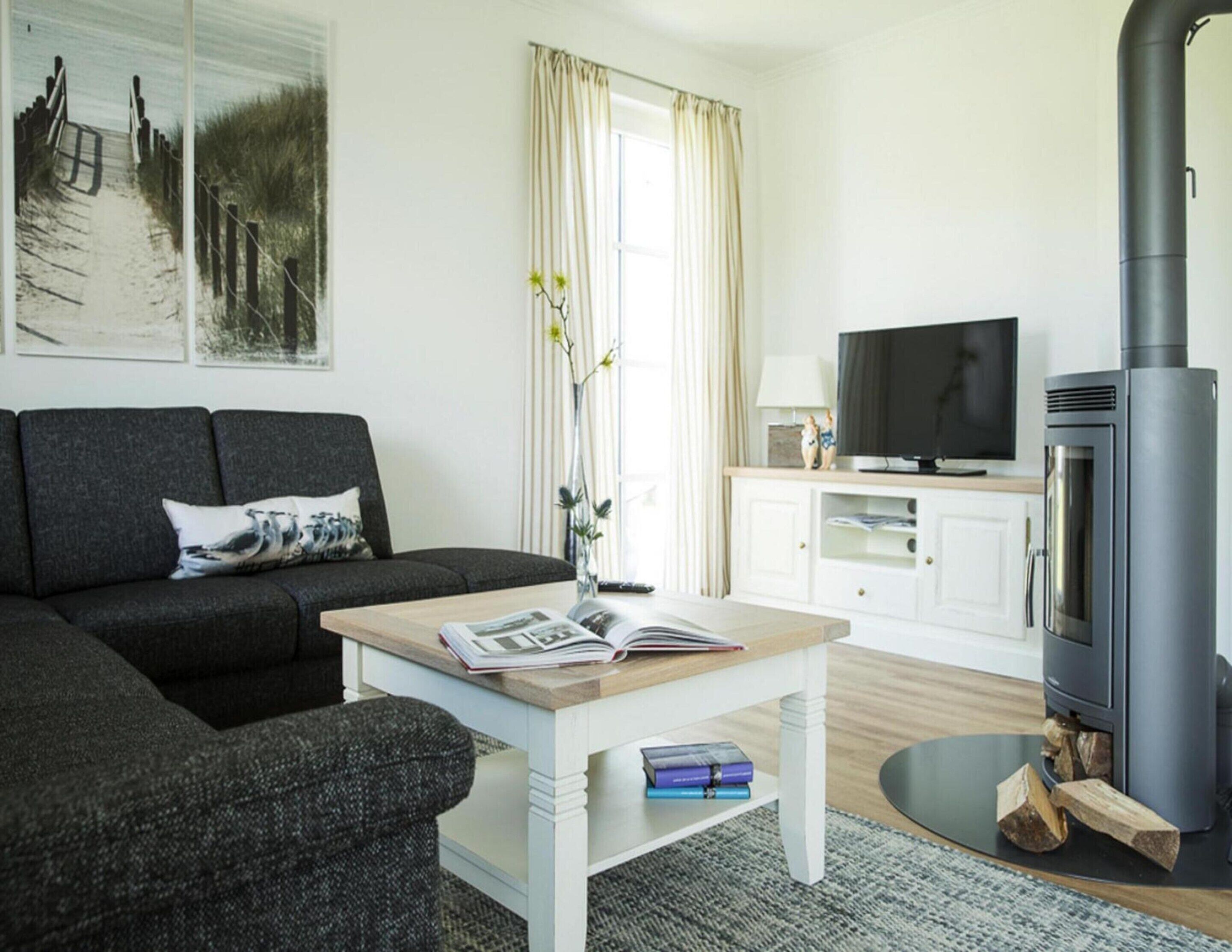 A modern living room with a sofa, a coffee table with books, a television, and a wood-burning stove.