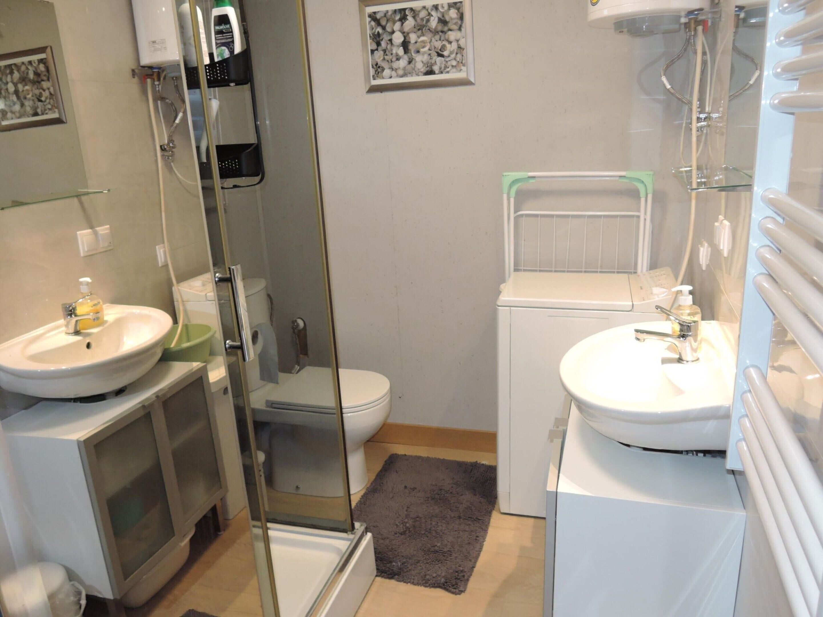 Une salle de bain compacte avec deux lavabos, des toilettes, un espace douche et un petit tapis.