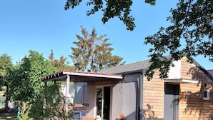 A small house with a covered patio, a lawn, and a dog. - Holiday Home in Nowe Warpno by the Harbor (Nowe Warpno)