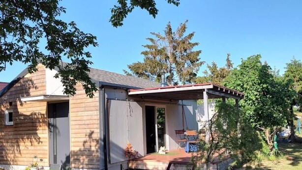 A single-story wooden house with a covered porch and a small garden area. - Holiday Home in Nowe Warpno by the Harbor (Nowe Warpno)