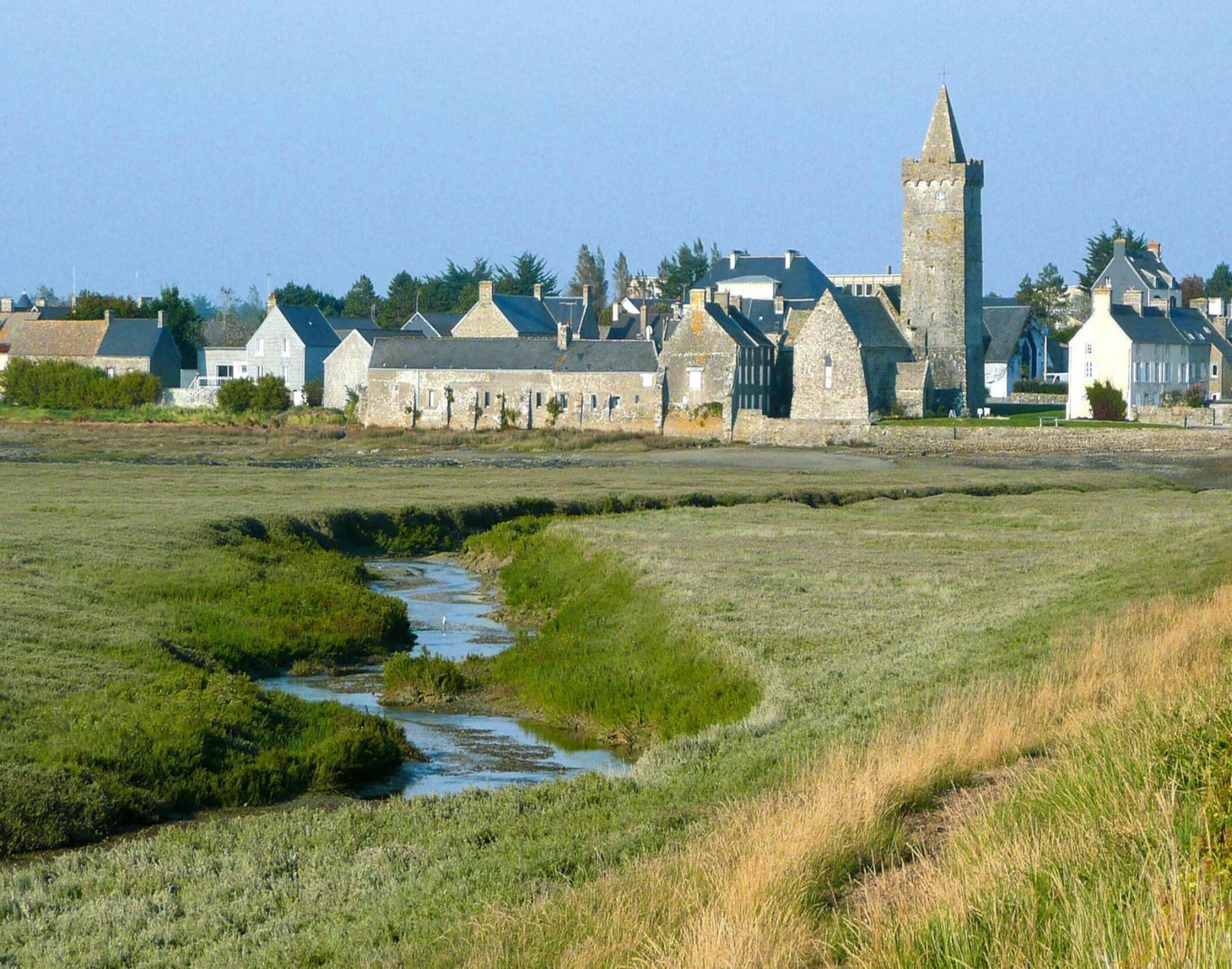 A rural landscape with stone buildings, a prominent tower, and a small stream.