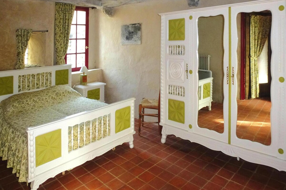 Un dormitorio con cama, armario, silla y ventana con cortinas.