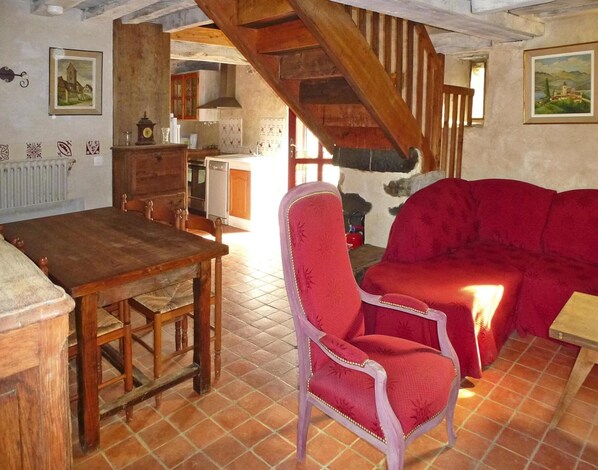 A rustic room with a wooden dining table, a red upholstered sofa, and a chair. There is a staircase leading to an upper level. - Manor Near Mont St. Michel and Contentin Beaches (Port-Bail-sur-Mer)