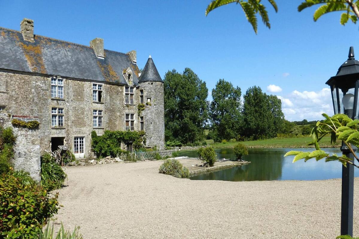 A historic stone building with multiple windows and a pond in the foreground.