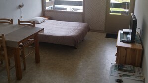 A small room with a bed, a desk, and a window with a view of a road and mountains. - Studio apartment at the foot of the slopes (St Aventin)