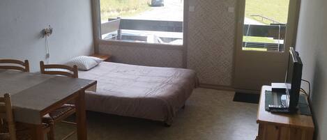 A small room with a bed, a desk, and a window with a view of a road and mountains.