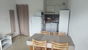 A compact kitchen with white cabinets, a microwave, and a refrigerator. There is a dining table with four chairs and a small side table. - Studio apartment at the foot of the slopes (St Aventin)