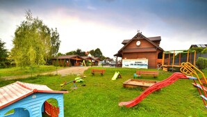 Ein Spielplatz mit verschiedenen Spielgeräten, einem hölzernen Gebäude mit einem Schild und einem blauen Spielhäuschen.