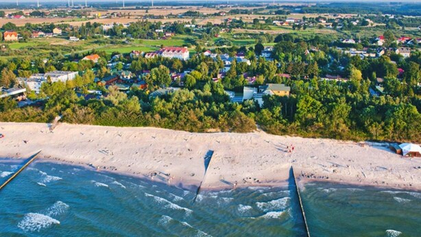 Eine Küstenstadt mit Strand, Häusern und Windkraftanlagen in der Ferne.