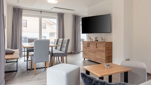 A modern hotel room with a dining area, a flat-screen TV, and a wooden cabinet with decorative items. - Chalet Arber in St.englmar With its own Hottube (Sankt Englmar)