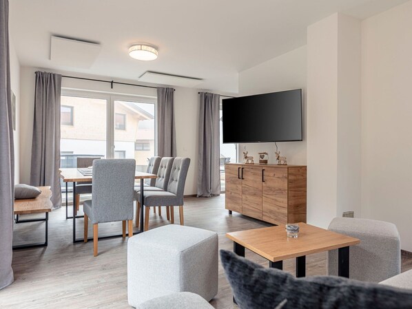 A modern hotel room with a dining area, a flat-screen TV, and a wooden cabinet with decorative items. - Chalet Arber in St.englmar With its own Hottube (Sankt Englmar)