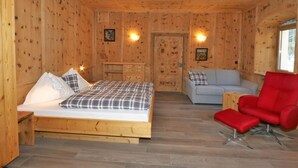 A wooden cabin room with a bed, a sofa, a red chair, and a small table. - Apartment in Fugen Near Spieljochbahn (Fuegen)