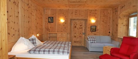 A wooden cabin room with a bed, a sofa, a red chair, and a small table.