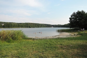 Ein See mit Schwimmern, umgeben von Wiesen und Bäumen.
