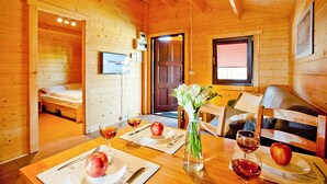 Interno di una baita in legno con un tavolo da pranzo apparecchiato per due persone, mele e bicchieri di vino.