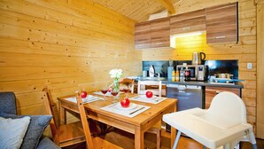 Un interno in legno con un tavolo da pranzo apparecchiato per due persone, un seggiolino e un angolo cottura con elettrodomestici.
