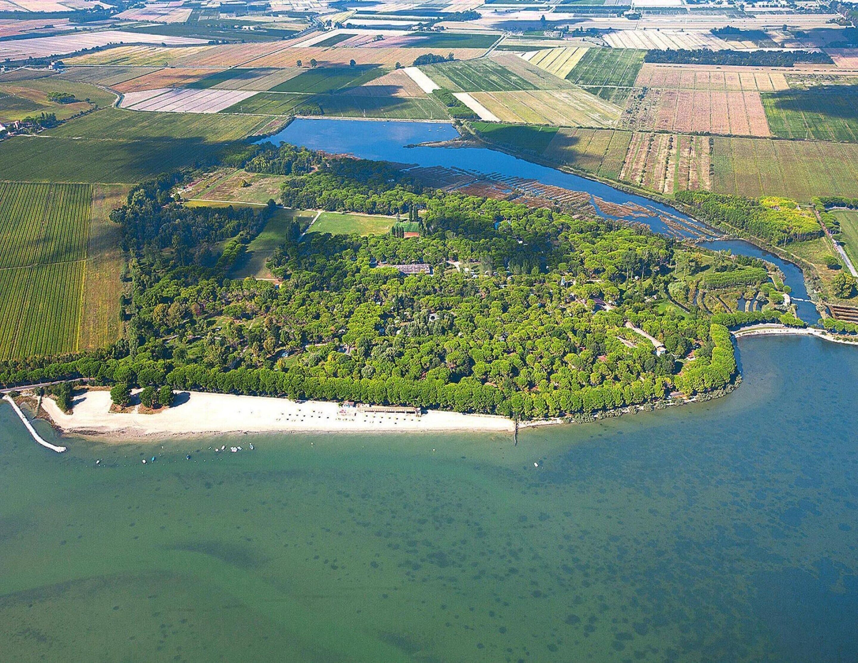 An aerial view of a coastal property with a dense forest, a sandy beach, and a large body of water.