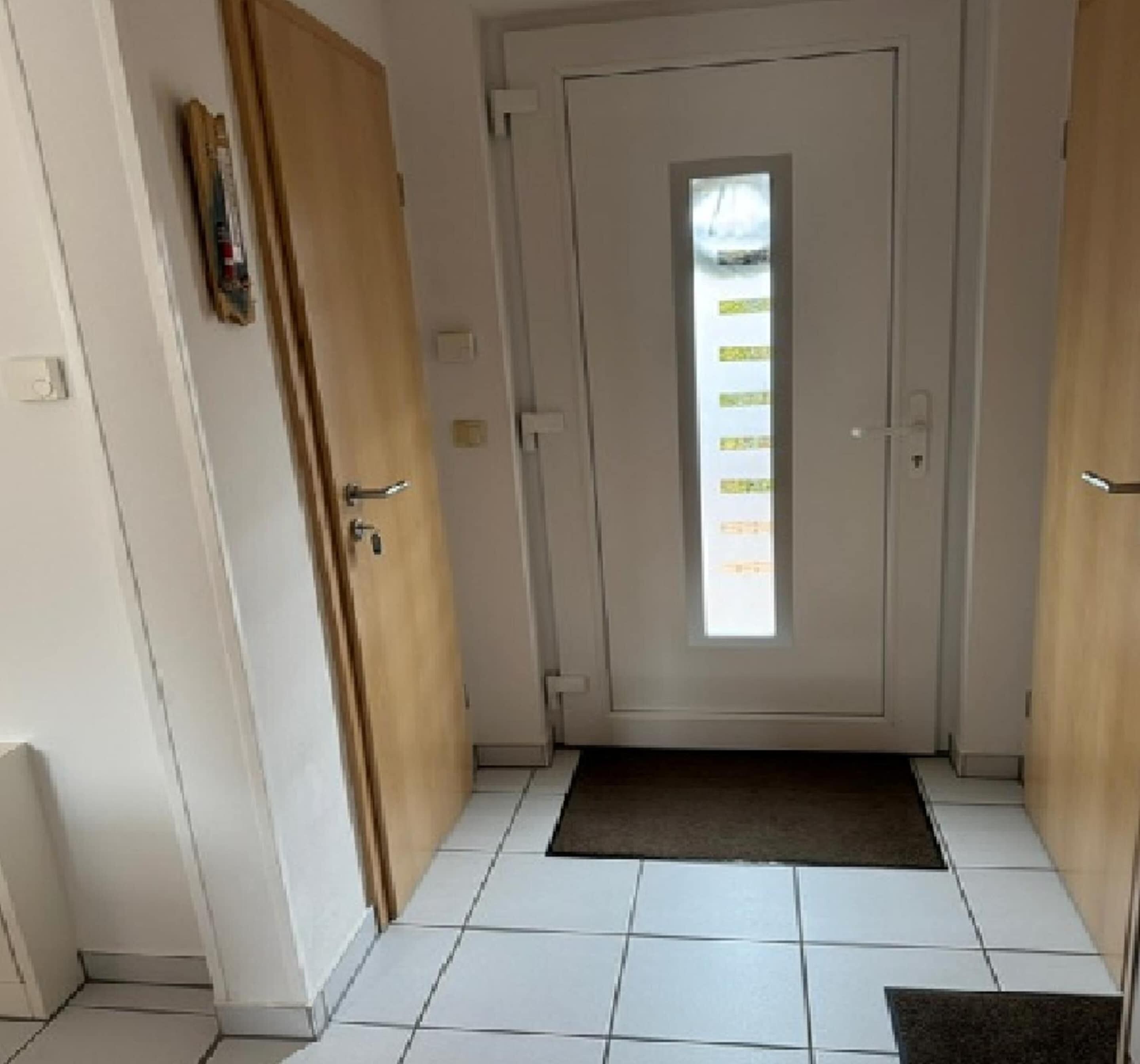 A hallway with a white door, a small window, and a tiled floor.