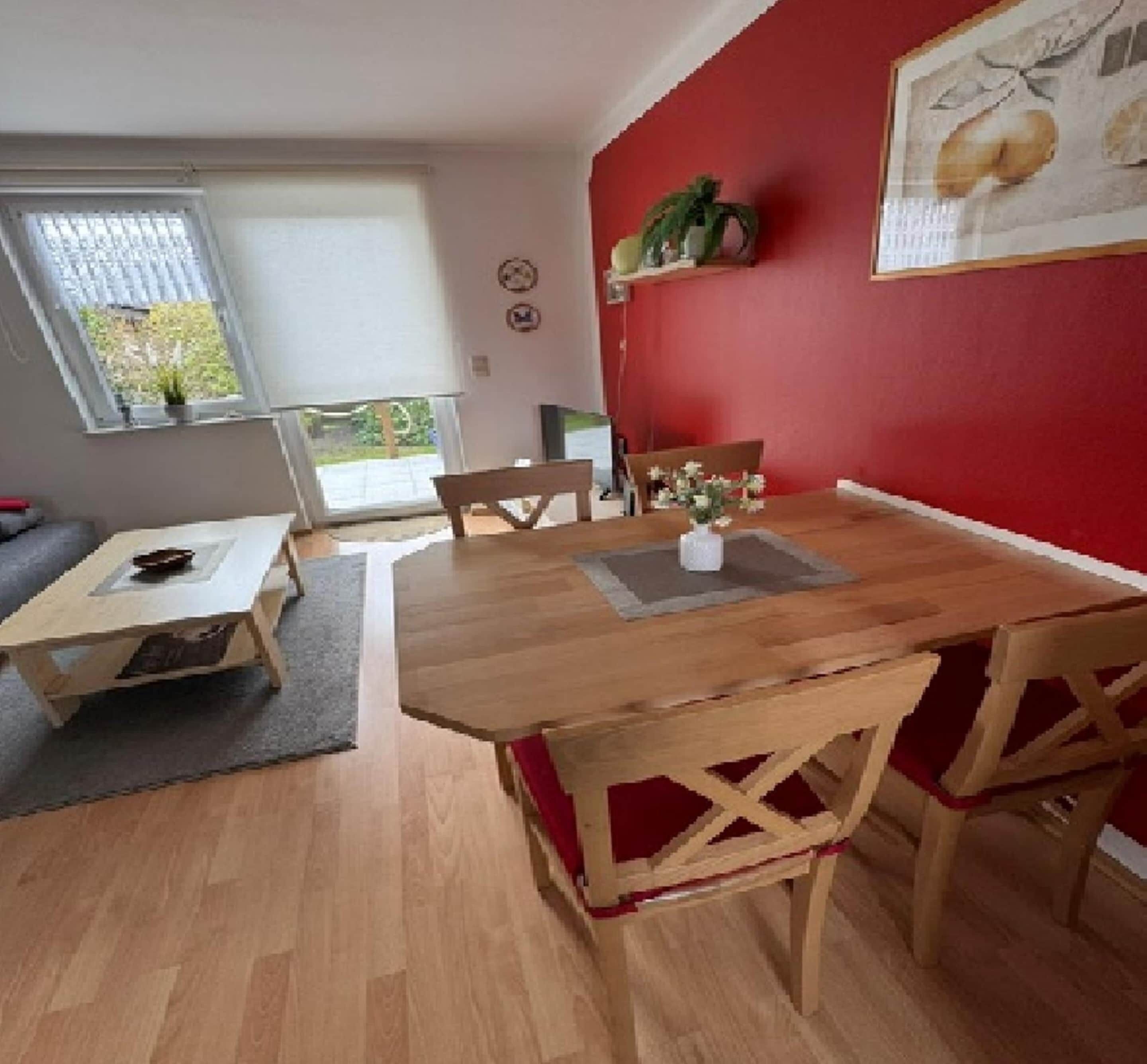 Un coin repas avec une table et des chaises en bois, une petite plante accrochée au mur et une fenêtre avec des stores.