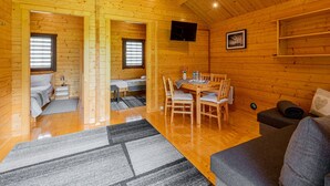 Interior acollidor d'una cabana amb un paviment de fusta, una zona de menjador amb taula i cadires, un sofà i un televisor fixat a la paret.