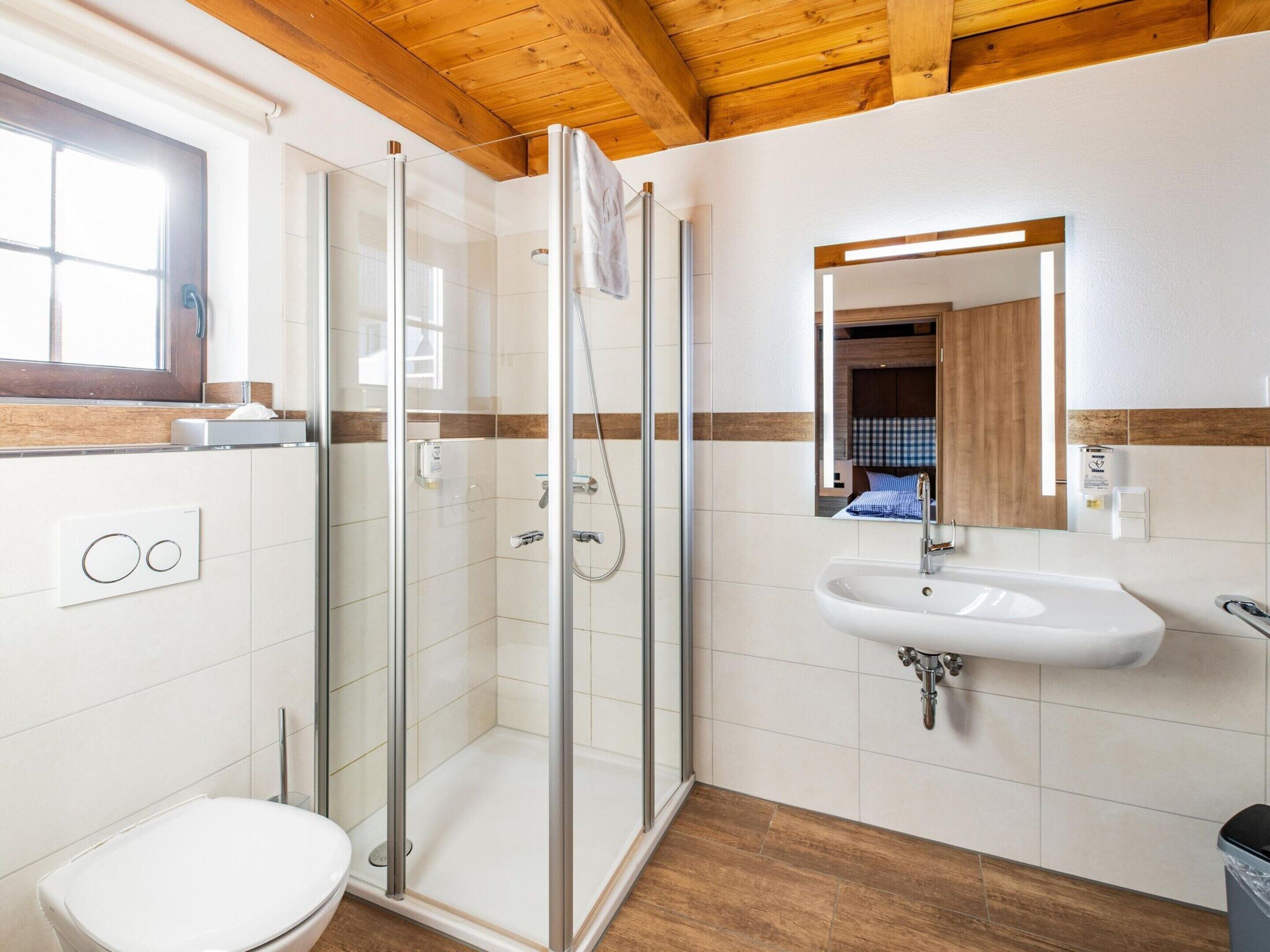 A modern bathroom with a glass-enclosed shower, a white sink, and a wooden ceiling.