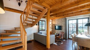 A spacious living area with a wooden staircase, a stone wall, a flat-screen TV, and a dining area with a table and chairs. - Chalets am Diemelsee in Heringhausen (Diemelsee)