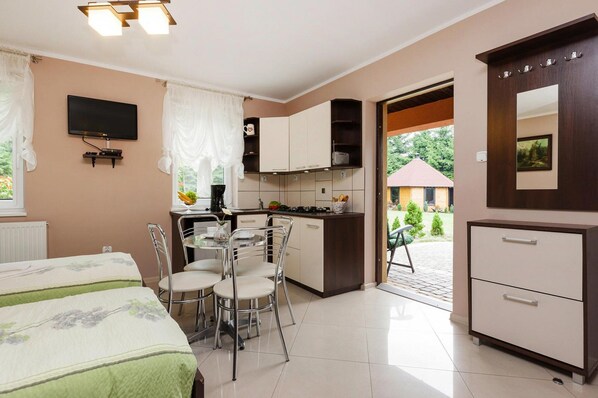 A compact hotel room with a kitchenette, a dining area with four chairs, a bed with floral bedding, a TV mounted on the wall, and a large mirror. - House Near Baltic Sea and Wolinski Park (gmina Wolin)