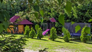 A playground with a swing set and a slide, surrounded by small trees and a wooden structure with a red roof. - House Near Baltic Sea and Wolinski Park (gmina Wolin)