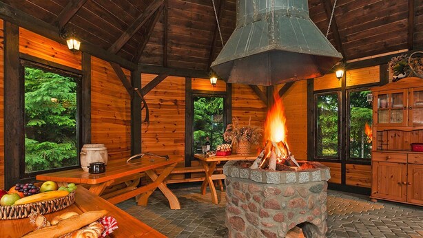 A rustic wooden interior with a stone fireplace, wooden furniture, and a view of greenery outside. - House Near Baltic Sea and Wolinski Park (gmina Wolin)