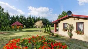 A two-story building with a red roof, surrounded by a well-maintained garden with red flowers and green shrubs. - House Near Baltic Sea and Wolinski Park (gmina Wolin)