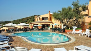 A pool area with lounge chairs, umbrellas, and a building with a tiled roof. - Apartment in Budoni With Terrace (Budoni)