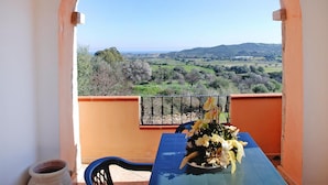 A balcony with a table and chairs, a vase of flowers, and a view of a green landscape with trees and hills. - Apartment in Budoni With Terrace (Budoni)