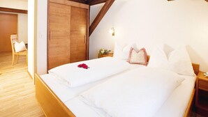 A bedroom with a wooden ceiling, a bed with white linens, a nightstand, and a chair. - Apartment in Ischgl Overlooking the Mountains (Ischgl)