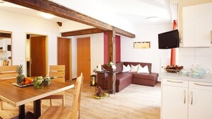 A modern living space with a wooden dining table, a sofa, a kitchen area, and a television mounted on the wall. - Apartment in Ischgl Overlooking the Mountains (Ischgl)