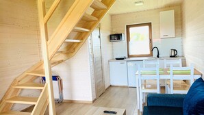 A compact wooden cabin with a kitchen area, a dining table with chairs, a staircase, and a sofa. - Two-story Holiday Homes Close to the Seaside Beach (Mielno)